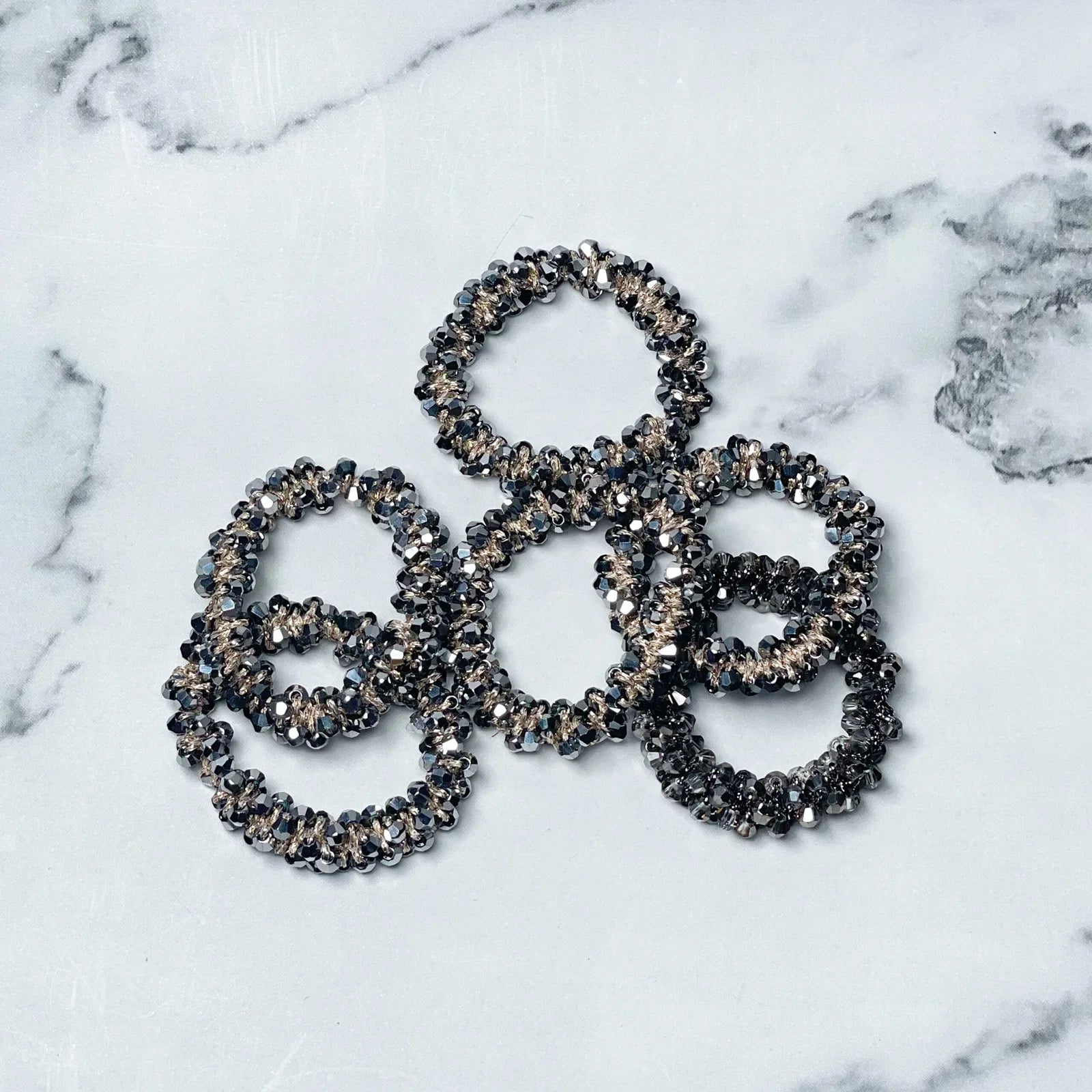 Set of crystal studded hair ties in black and silver tones on white marble background