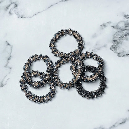 Set of crystal studded hair ties in black and silver tones on white marble background