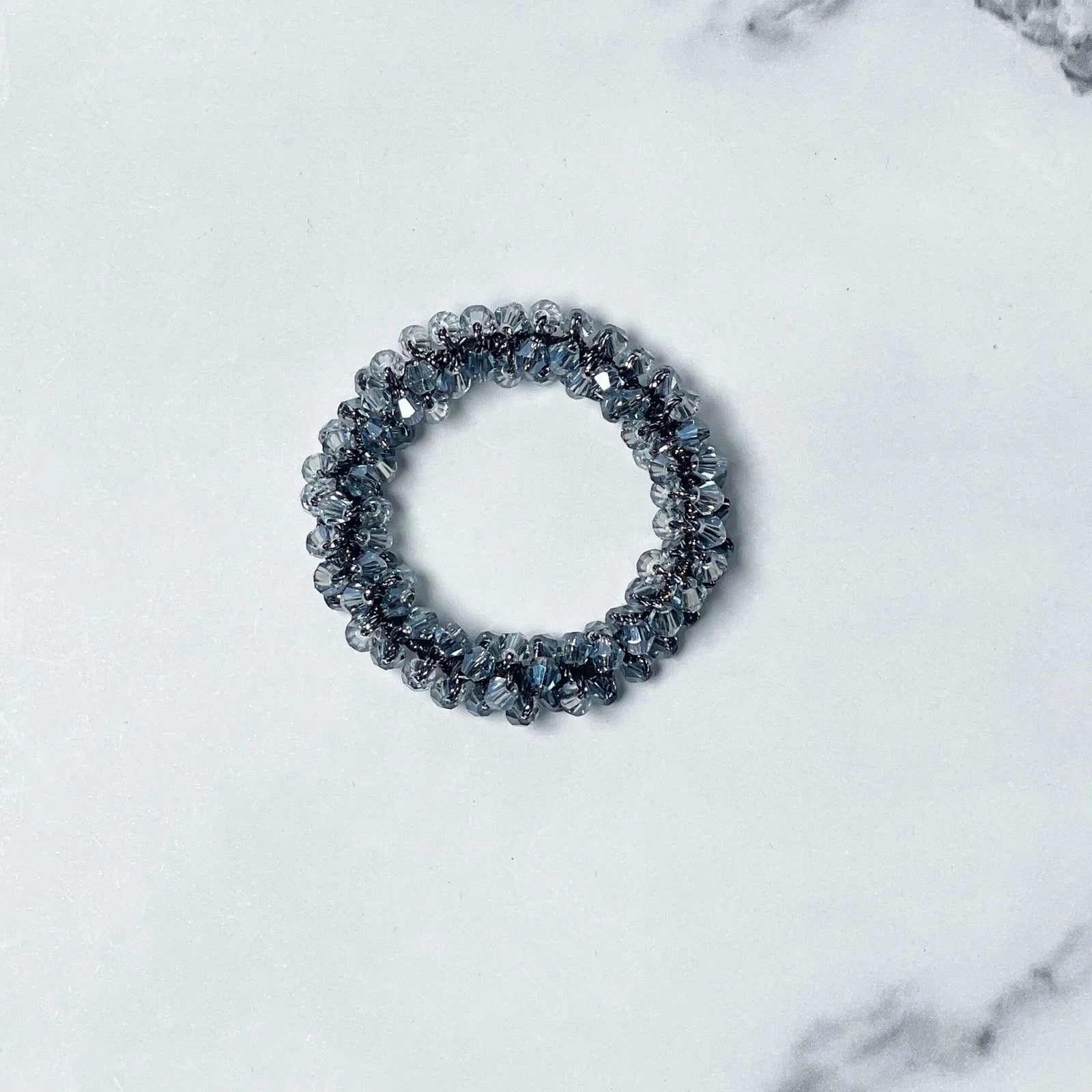 Crystal studded hair ties in a circular design with sparkling clear beads on a white marble surface
