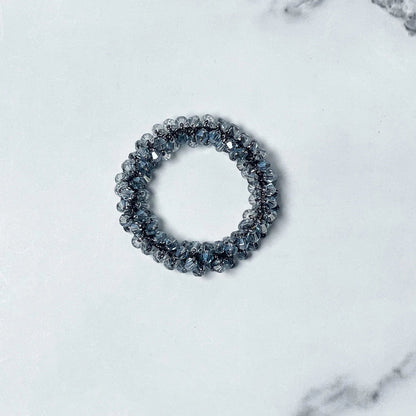 Crystal studded hair ties in a circular design with sparkling clear beads on a white marble surface