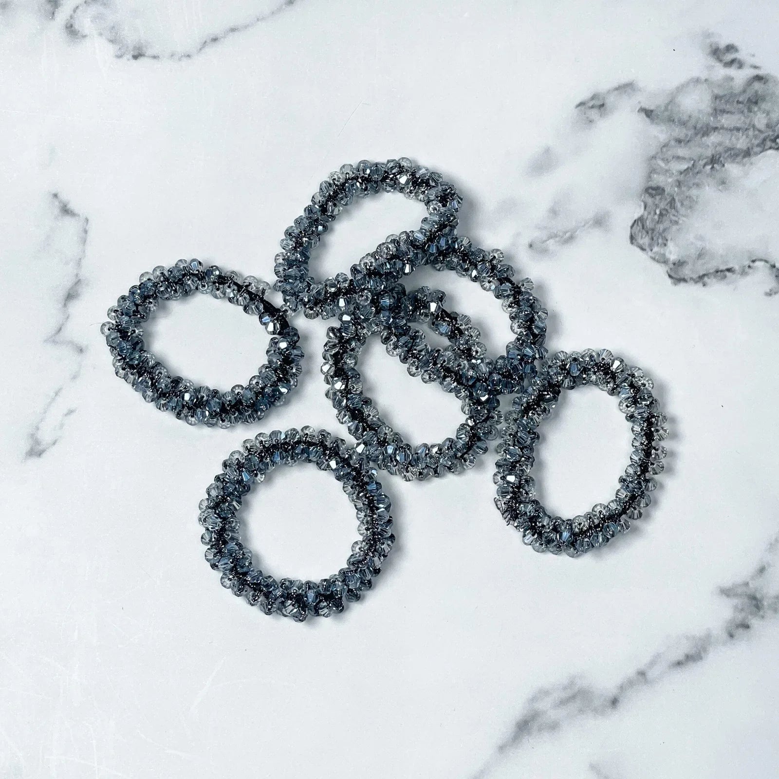 Set of black crystal studded hair ties on white marble background for stylish hair accessories