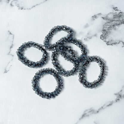 Set of black crystal studded hair ties on white marble background for stylish hair accessories