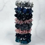 Stack of crystal studded hair ties in blue, black, gray, and pink colors on white background