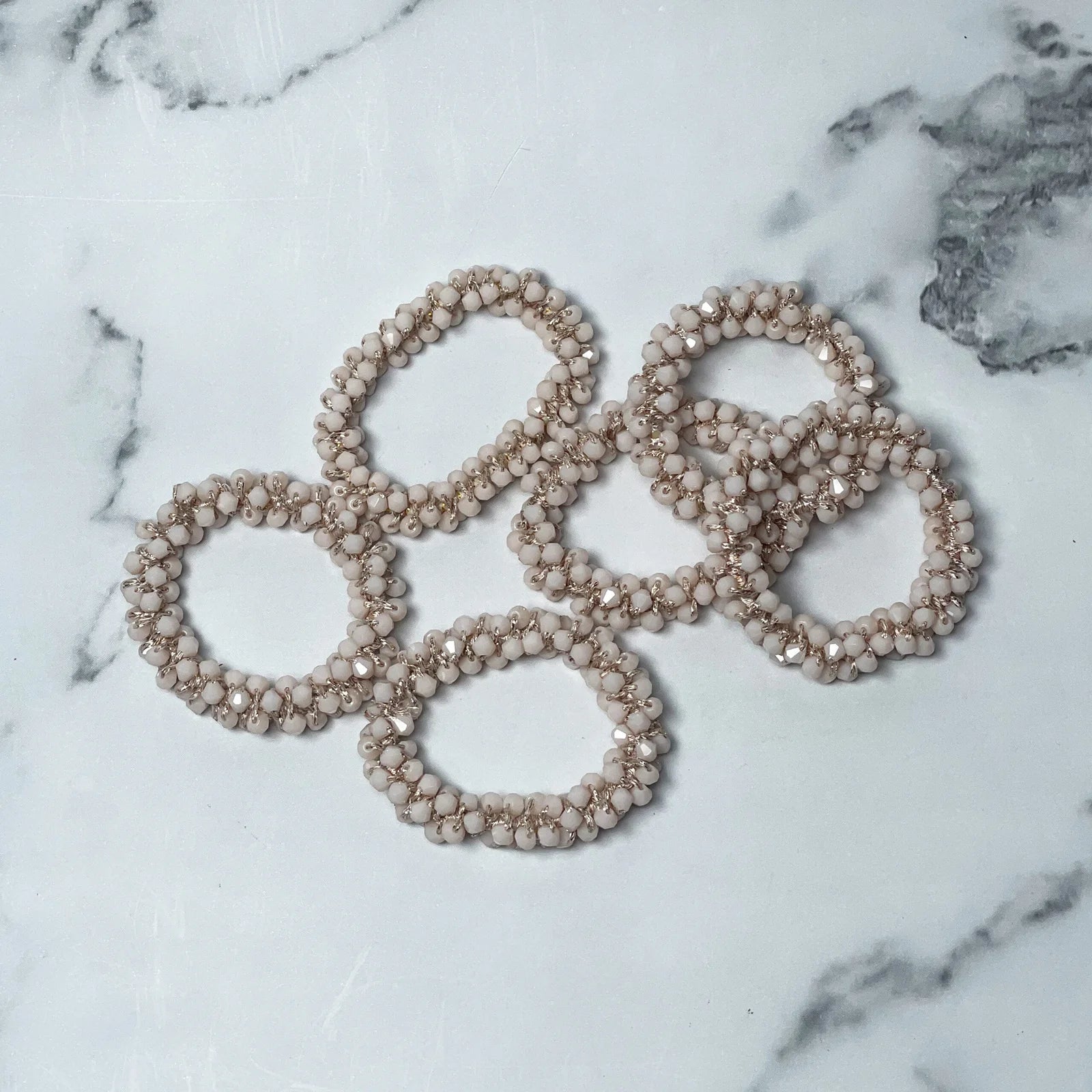 Crystal studded hair ties in neutral tones arranged on a white marble surface