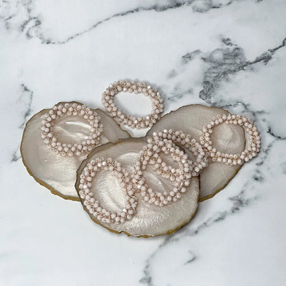 Set of beige crystal studded hair ties arranged on decorative marble coasters on white marble background