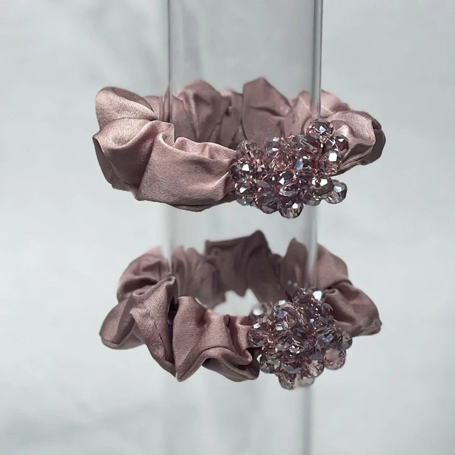 Pair of pink satin crystal studded hair ties with sparkling embellishments on a clear stand