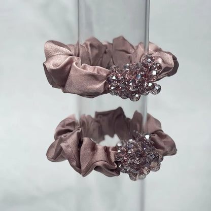 Pair of pink satin crystal studded hair ties with sparkling embellishments on a clear stand