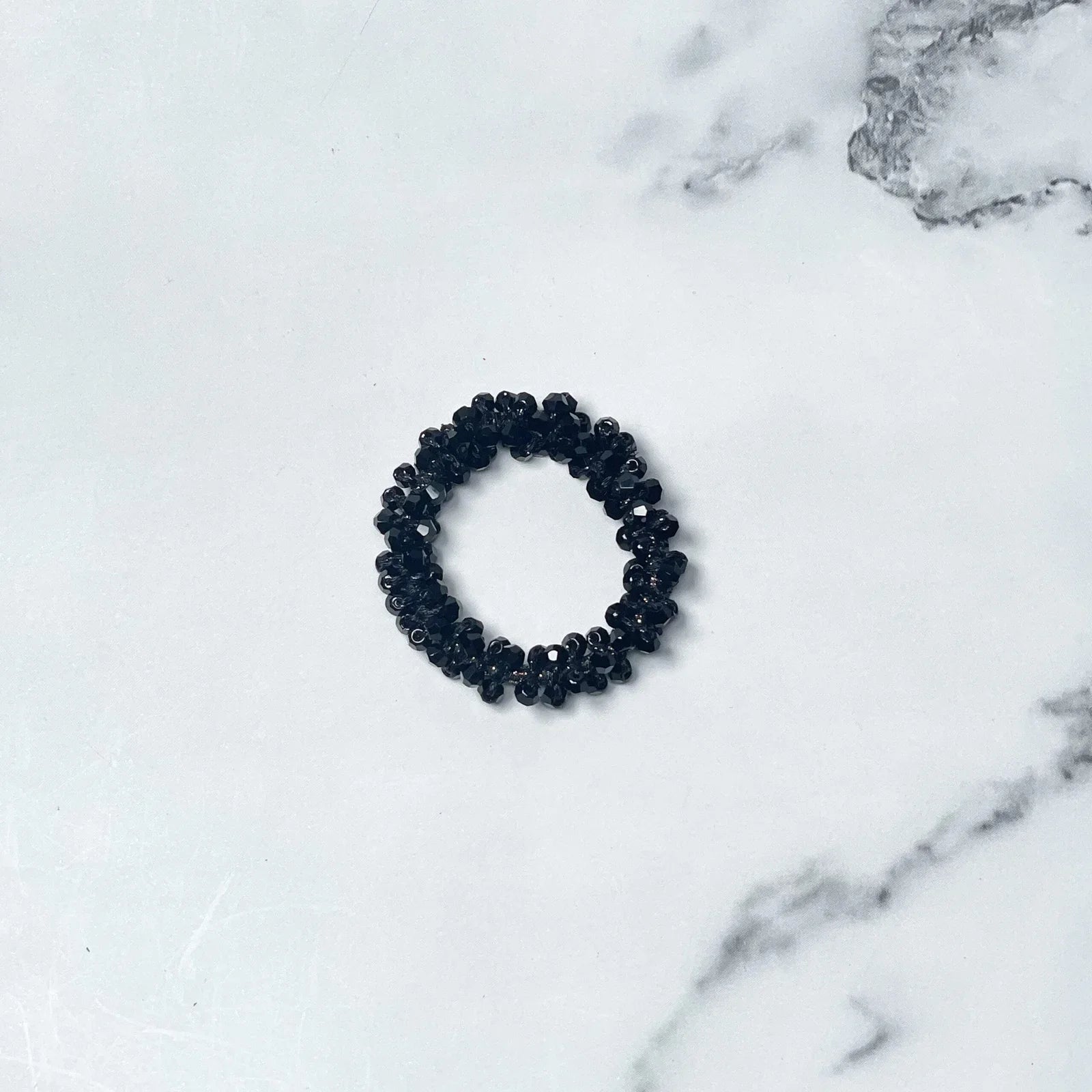 Black crystal studded hair ties with glossy beads on white marble background