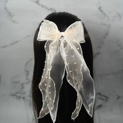 Dotted organza bow hair pin in cream color worn on dark hair with long flowing tails