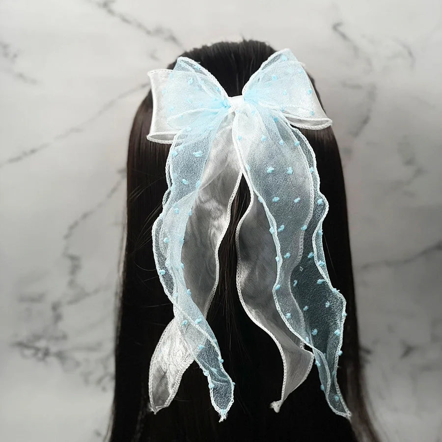 Light blue dotted organza bow hair pin attached to long dark hair against marble background