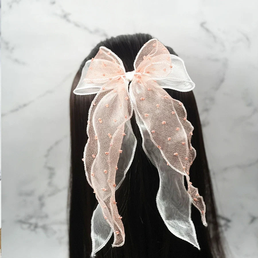 Dotted organza bow hair pin in soft pink with delicate fabric texture worn on dark straight hair
