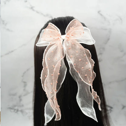 Dotted organza bow hair pin in soft pink with delicate fabric texture worn on dark straight hair