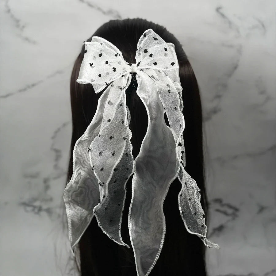White dotted organza bow hair pin with long flowing tails attached to dark hair