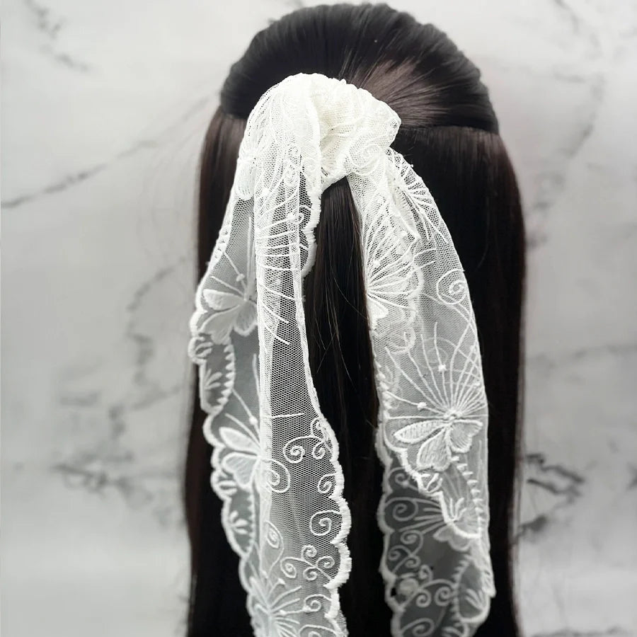 White embroidered lacy scarf tied in hair with intricate floral patterns and delicate fabric