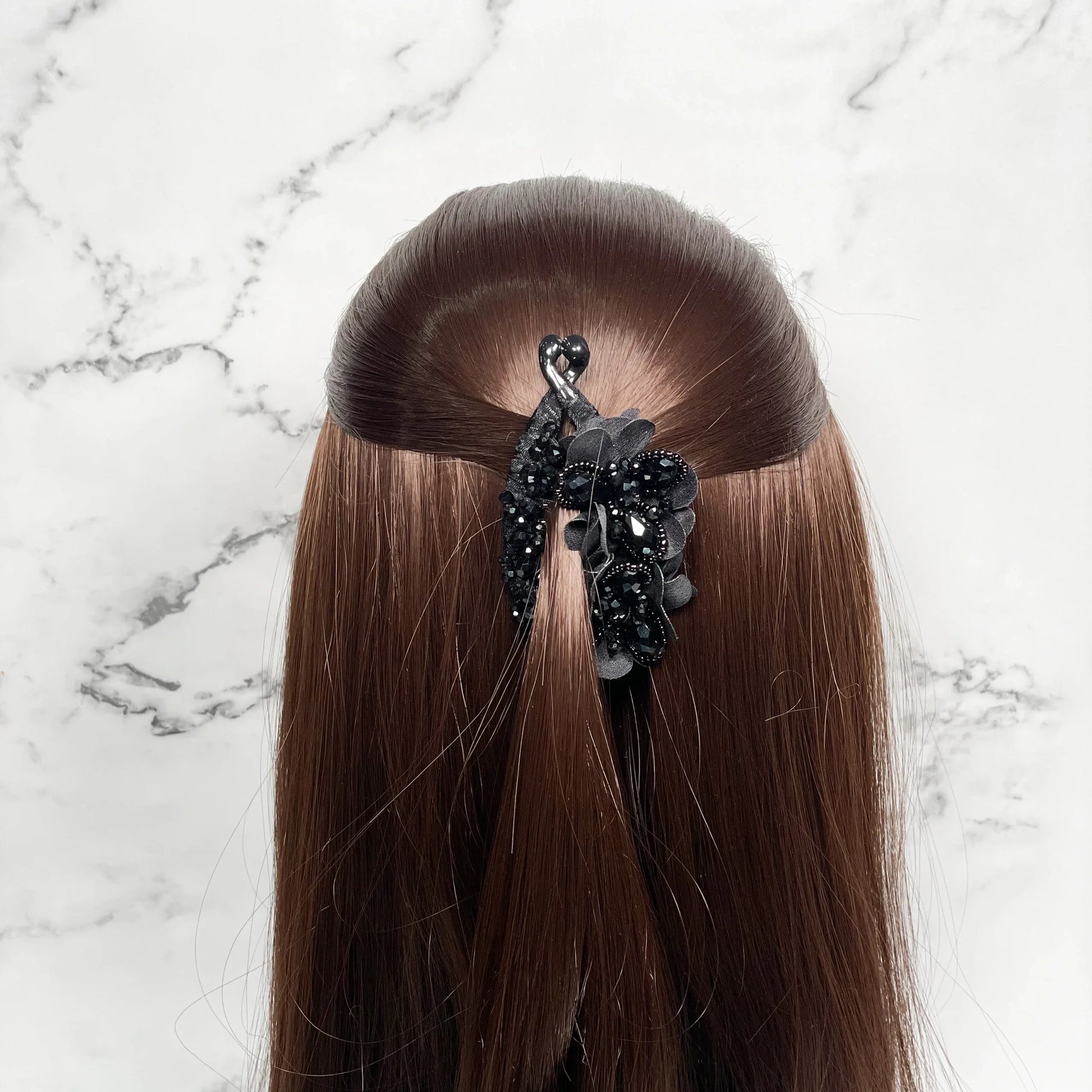 Black Floral and Crystal Studded Banana Clips holding long brown hair against marble background