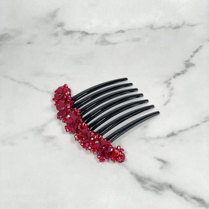 Black hair comb decorated with red floral beaded hair comb clips on white marble surface