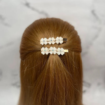 Two floral hair pins for women with white flowers and small decorative gems in brown hair