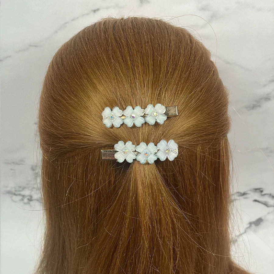 White floral hair pins for women clipped on light brown hair against a marble background