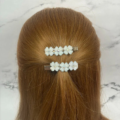 White floral hair pins for women clipped on light brown hair against a marble background