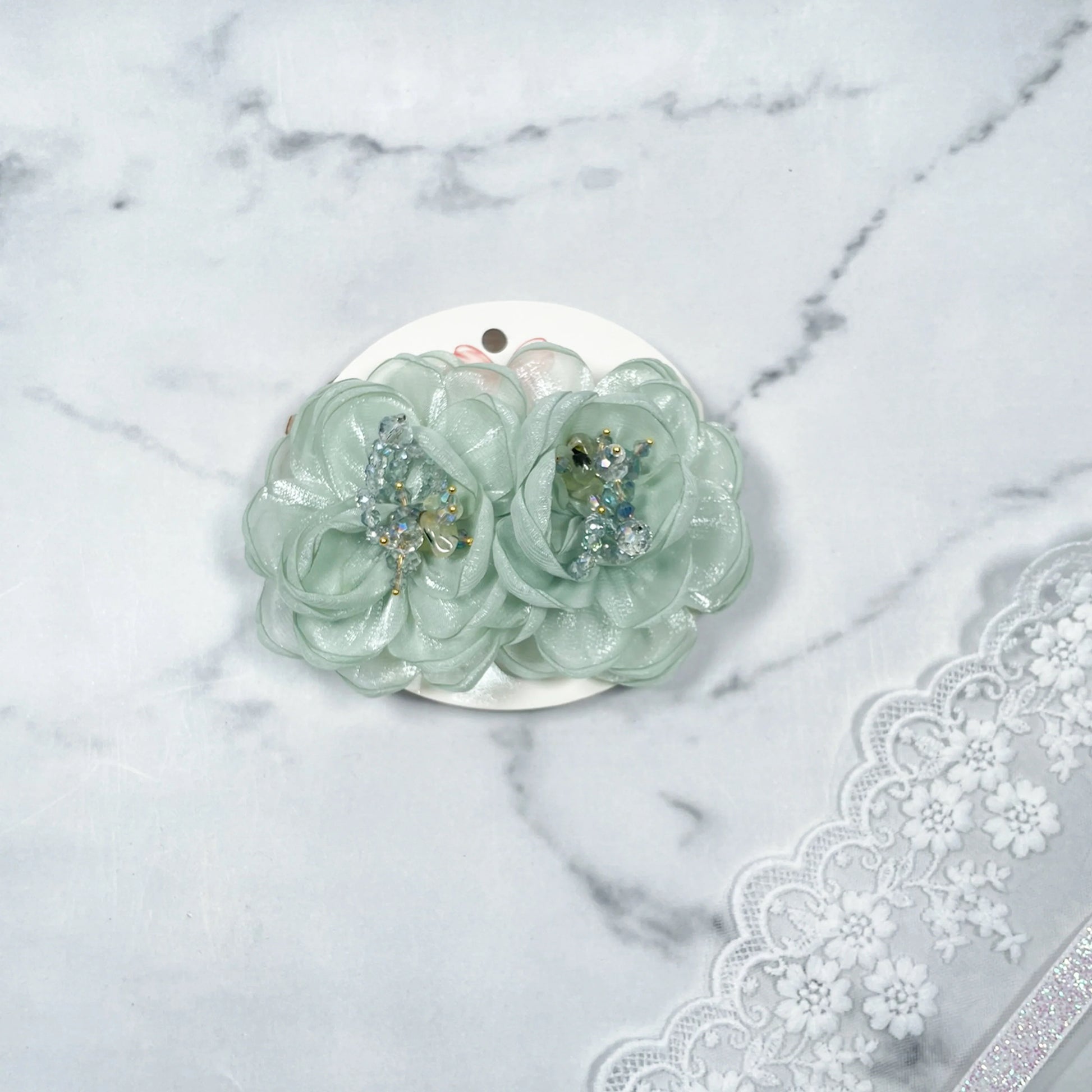 Mint green floral organza hair pins with bead embellishments on white card with lace background