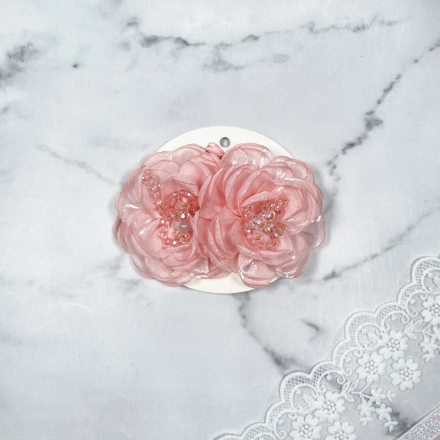Pink floral organza hair pins with bead embellishments displayed on white card over lace fabric background