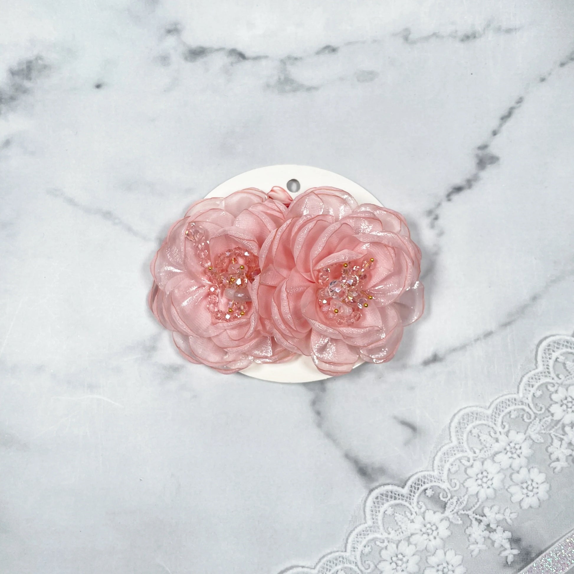 Pink floral organza hair pins with bead embellishments displayed on white card over lace fabric background