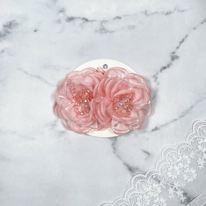 Pink floral organza hair pins with bead embellishments displayed on white card over lace fabric background