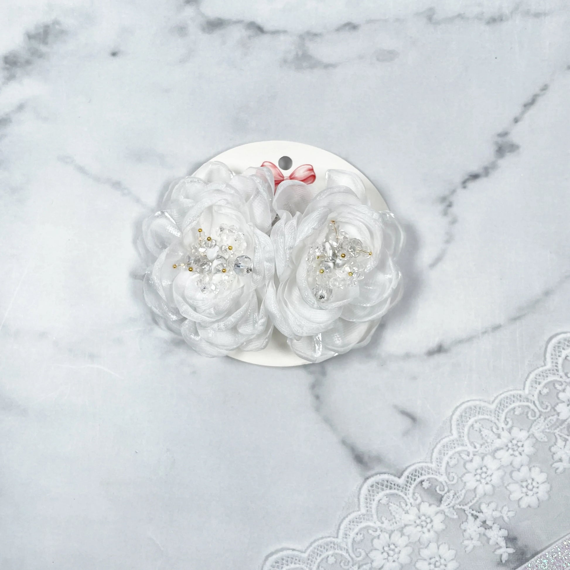 White floral organza hair pins with pearl and bead accents displayed on round white card