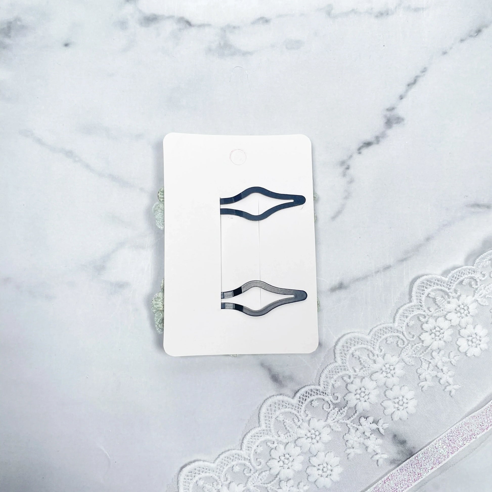 Two flower crystal hair pins displayed on a white card over a marble surface with lace detailing