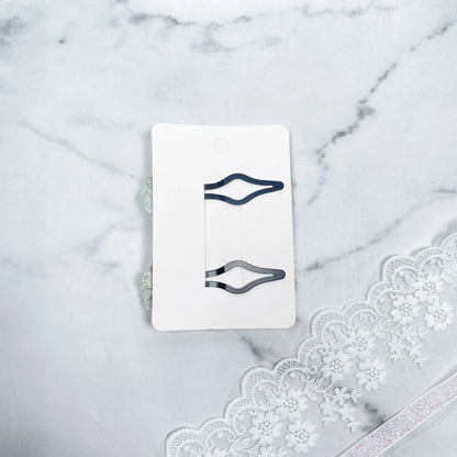 Two flower crystal hair pins displayed on a white card over a marble surface with lace detailing