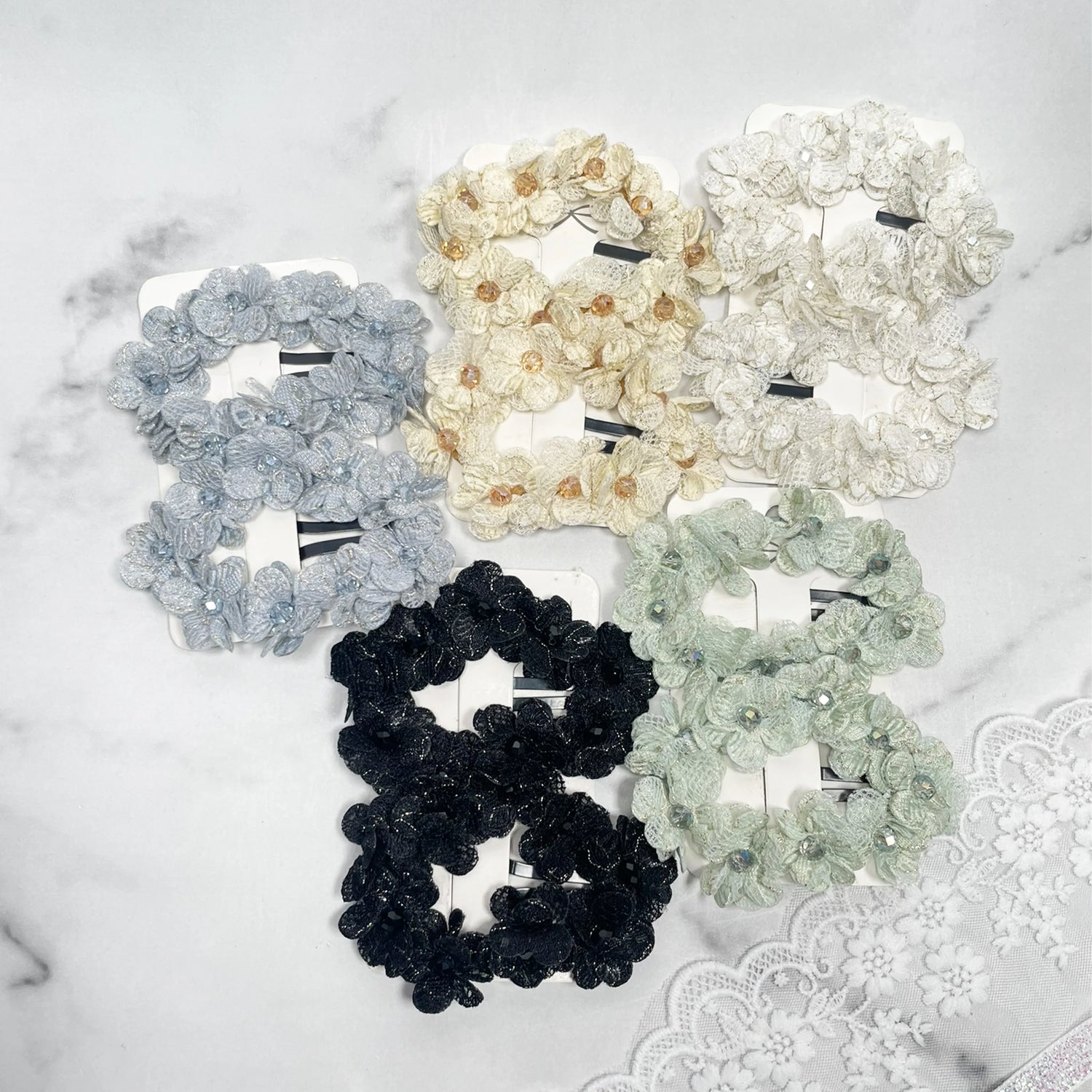 Set of flower crystal hair pins in various colors including black, white, cream, gray, and green on a marble surface
