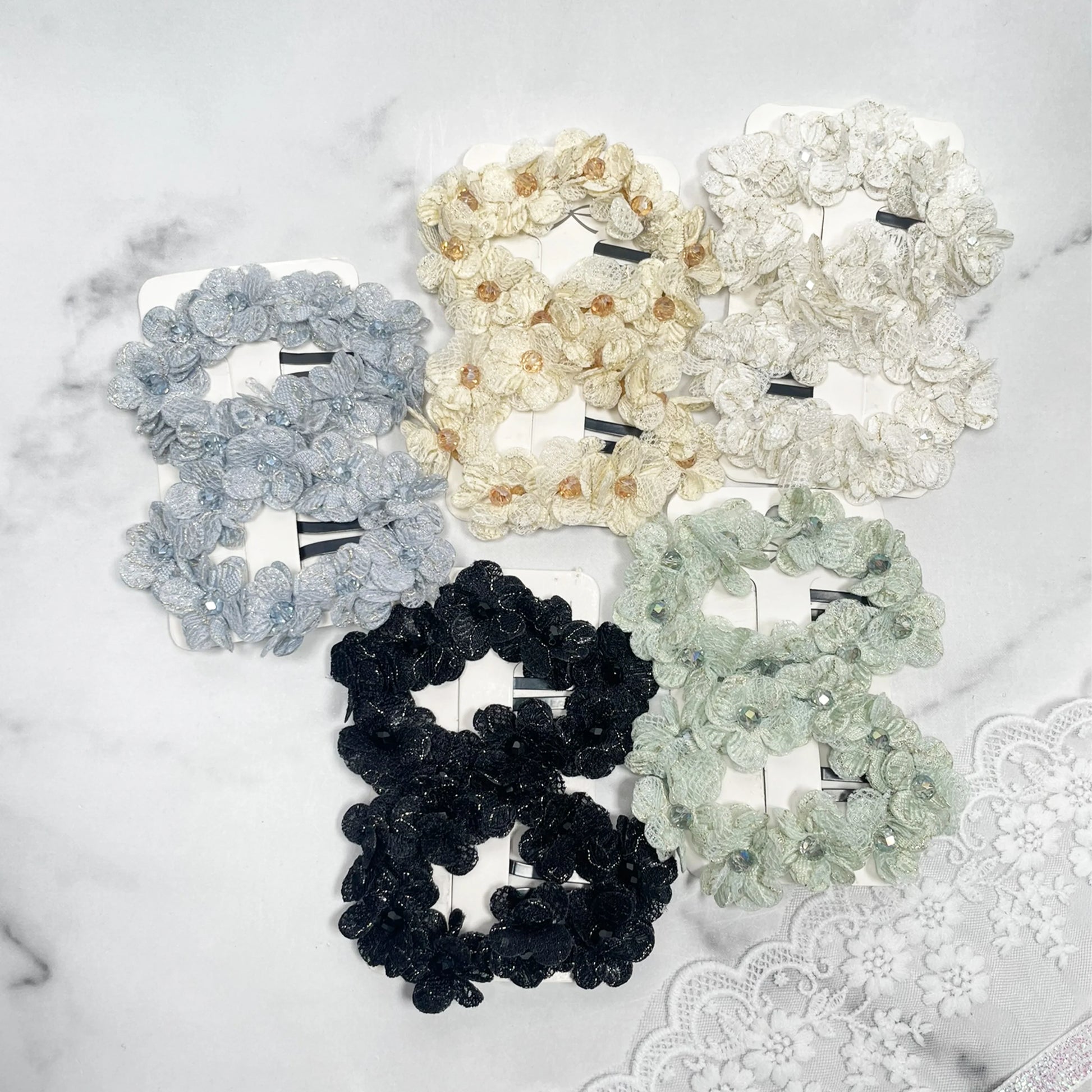 Set of flower crystal hair pins in various colors including black, white, cream, gray, and green on a marble surface