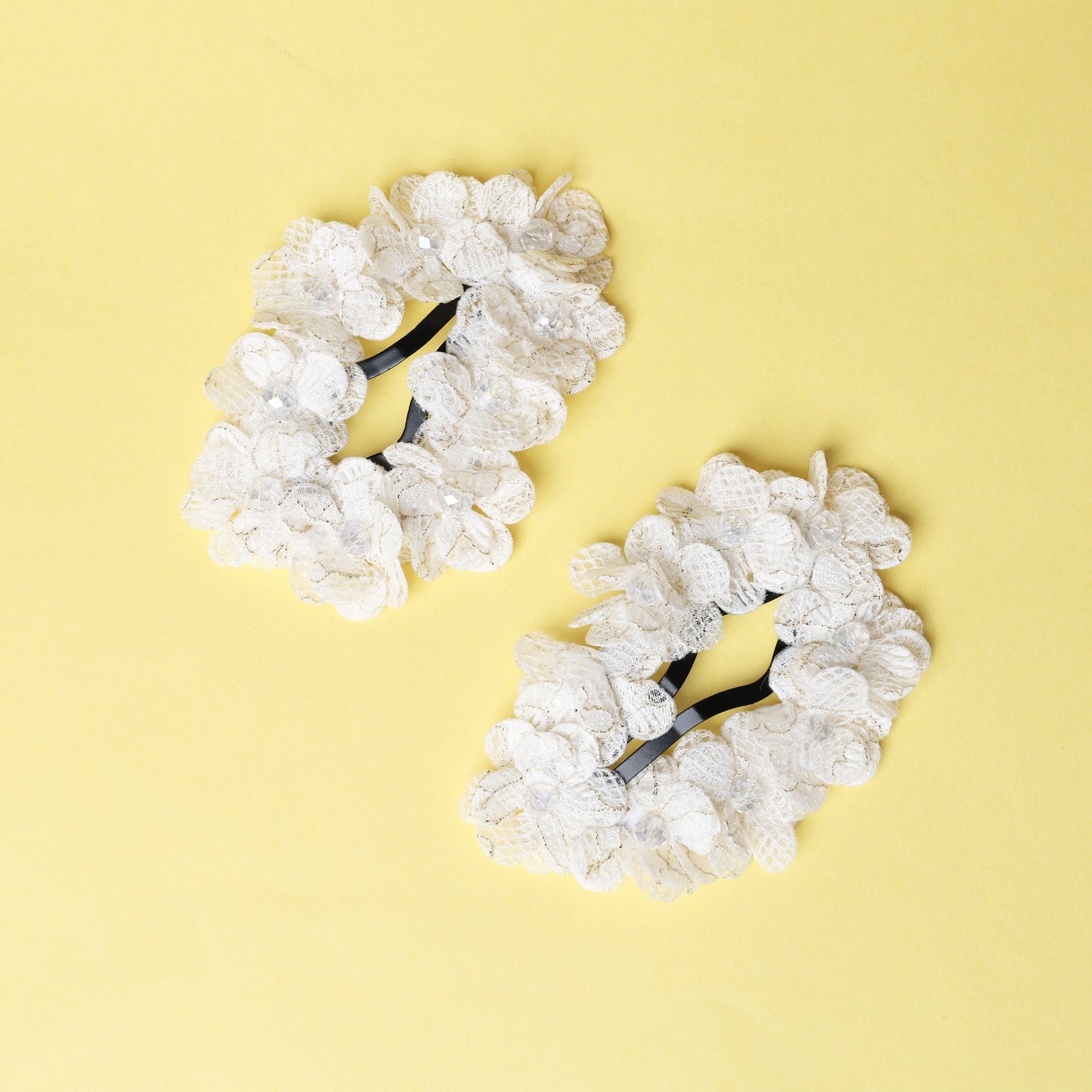 Pair of white lace flower crystal hair pins with delicate floral design on yellow background