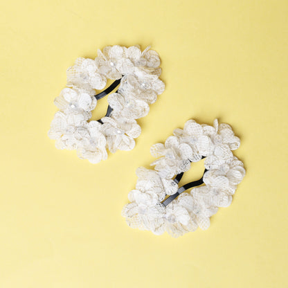 Pair of white lace flower crystal hair pins with delicate floral design on yellow background