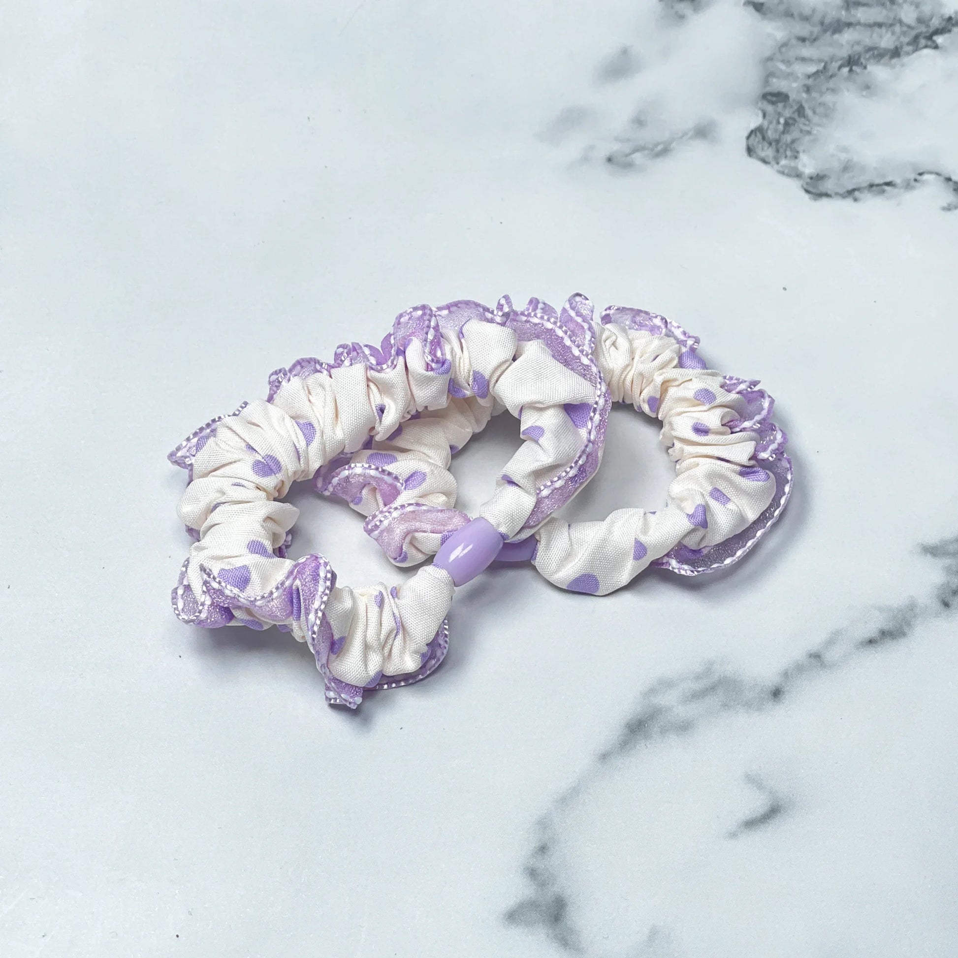 Set of frill polka dot hair ties in white with purple dots and lace edges on marble surface