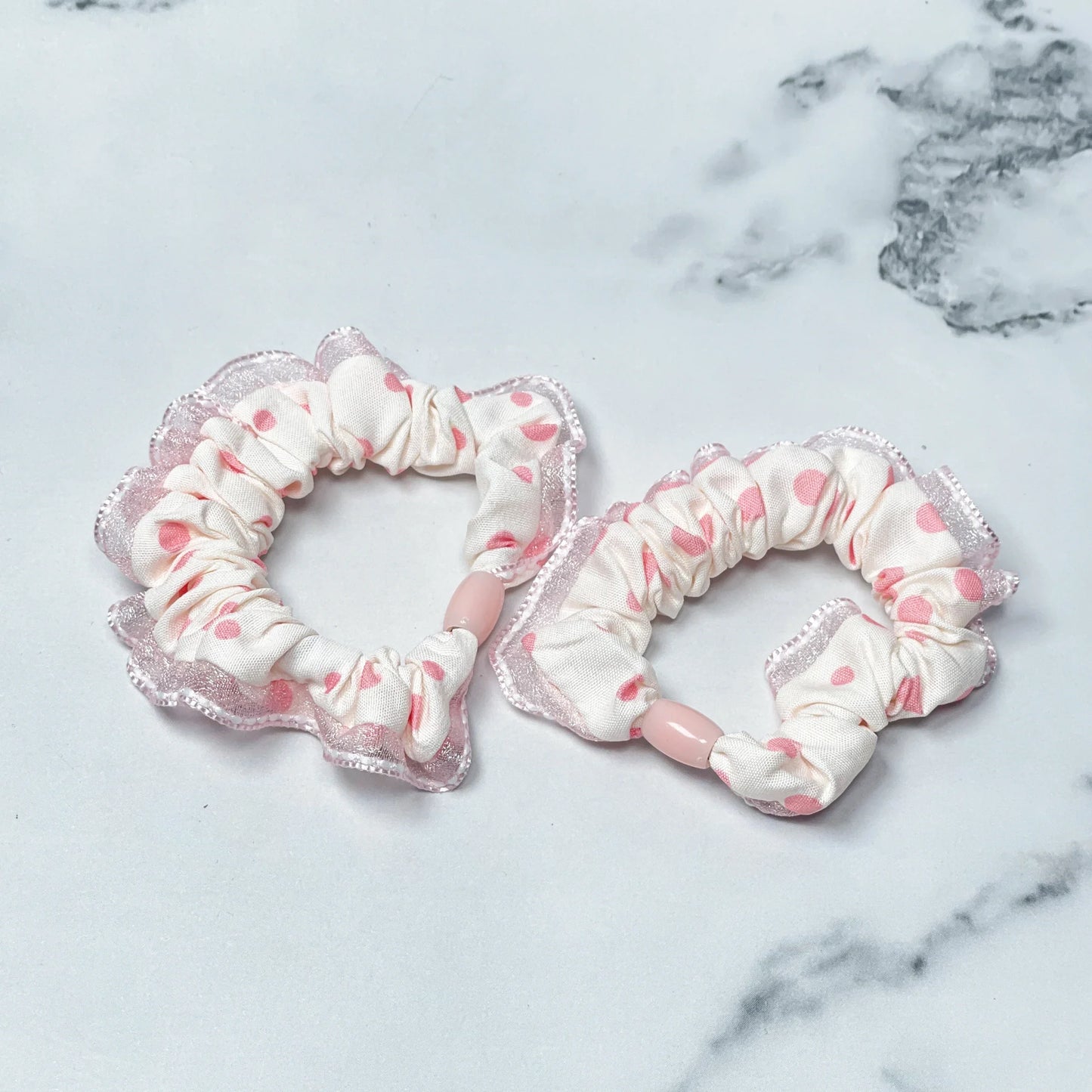 Set of frill polka dot hair ties in white with pink dots and lace edges on marble background
