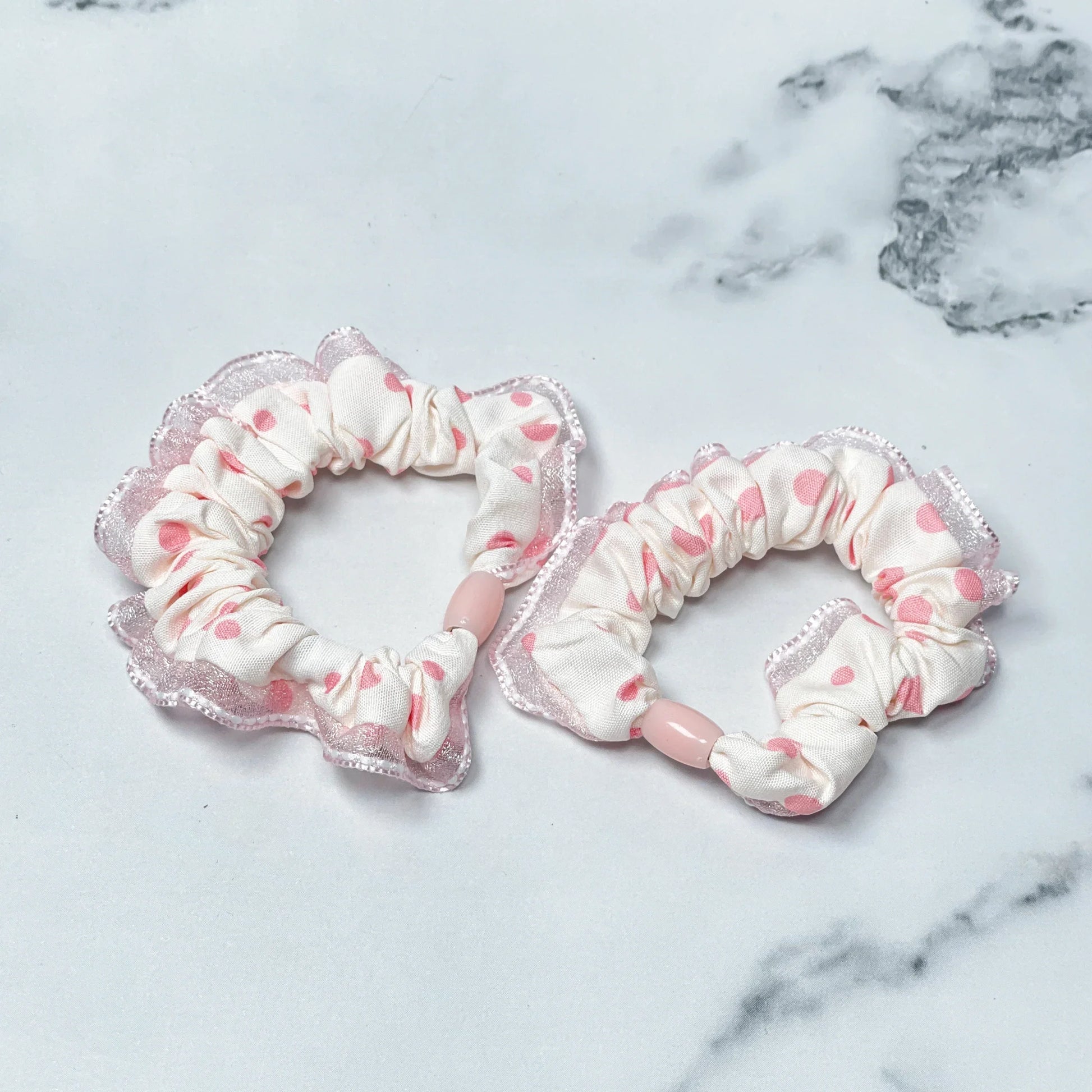 Set of frill polka dot hair ties in white with pink dots and lace edges on marble background