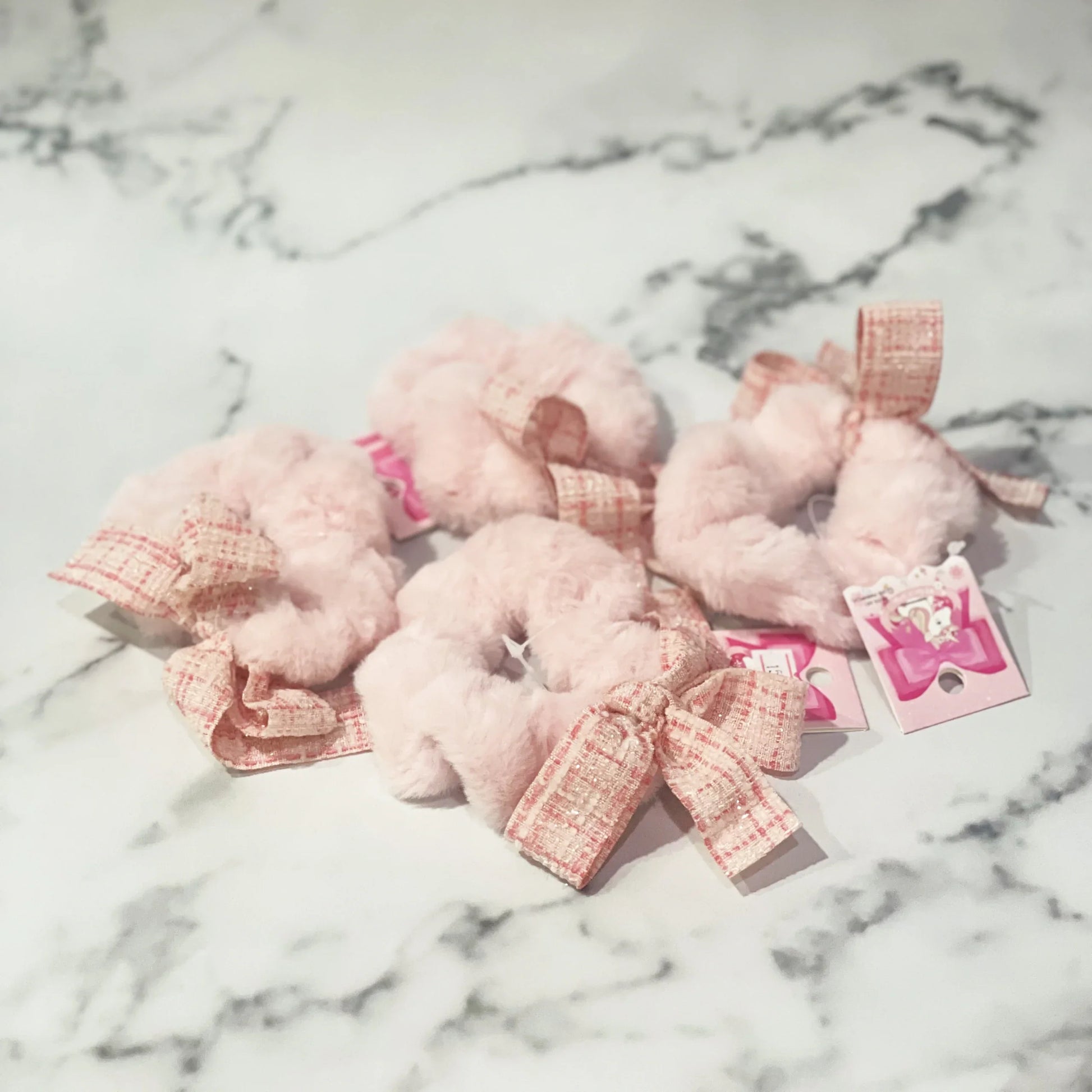 Pink fur scrunchie with check ribbon displayed on marble surface from mydevelopmentstor