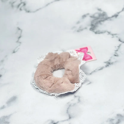 Beige fur scrunchies with lace trim displayed on marble surface for stylish hair accessories