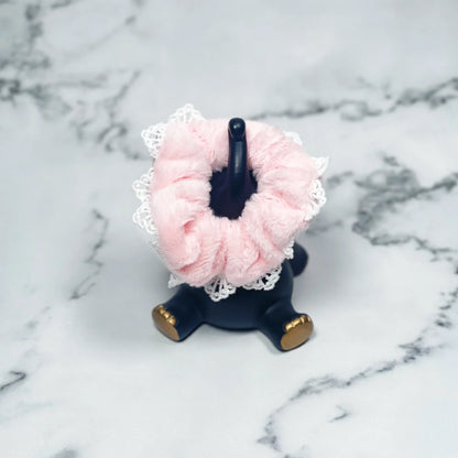 Pink fur scrunchies with lace displayed on a black hand-shaped holder on marble surface