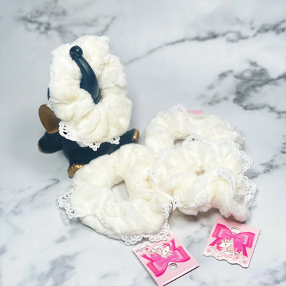 White fur scrunchies with lace edges displayed on a marble surface with pink tags