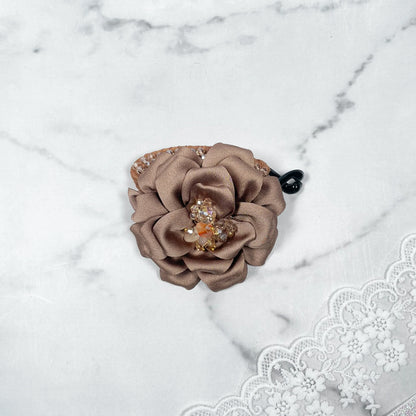 Bella Luxe golden crystal banana clip with decorative brown fabric flower on marble background