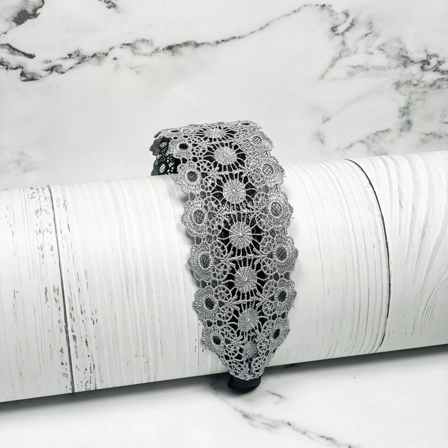 Grey lacy hairband with floral lace design displayed on white rustic wooden surface