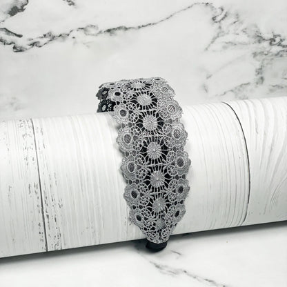 Grey lacy hairband with floral lace design displayed on white rustic wooden surface