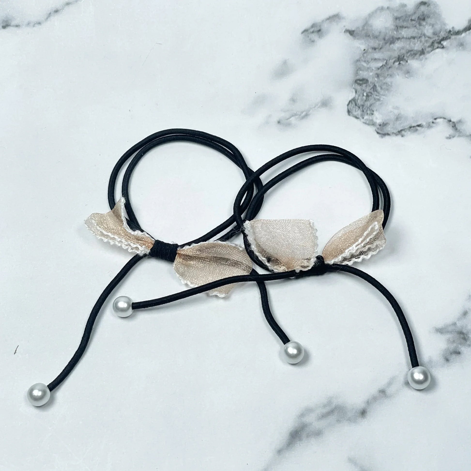 Black hair ties with bows and beads featuring beige fabric bows and white pearl-like beads