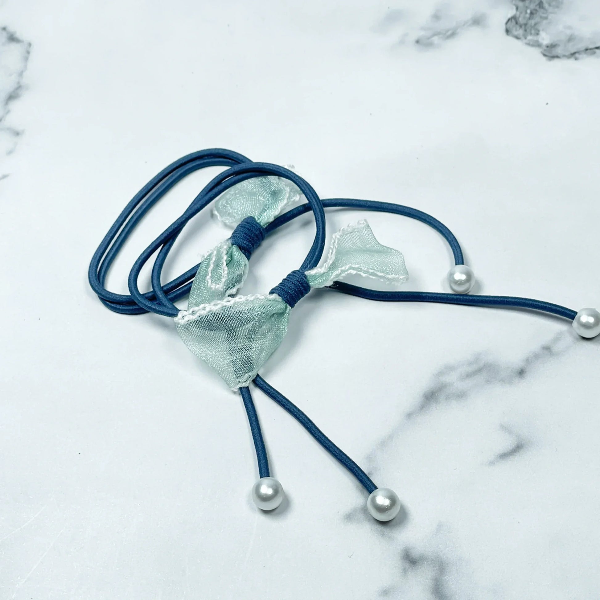 Blue hair ties with bows and beads featuring light green fabric bows and pearl-like beads