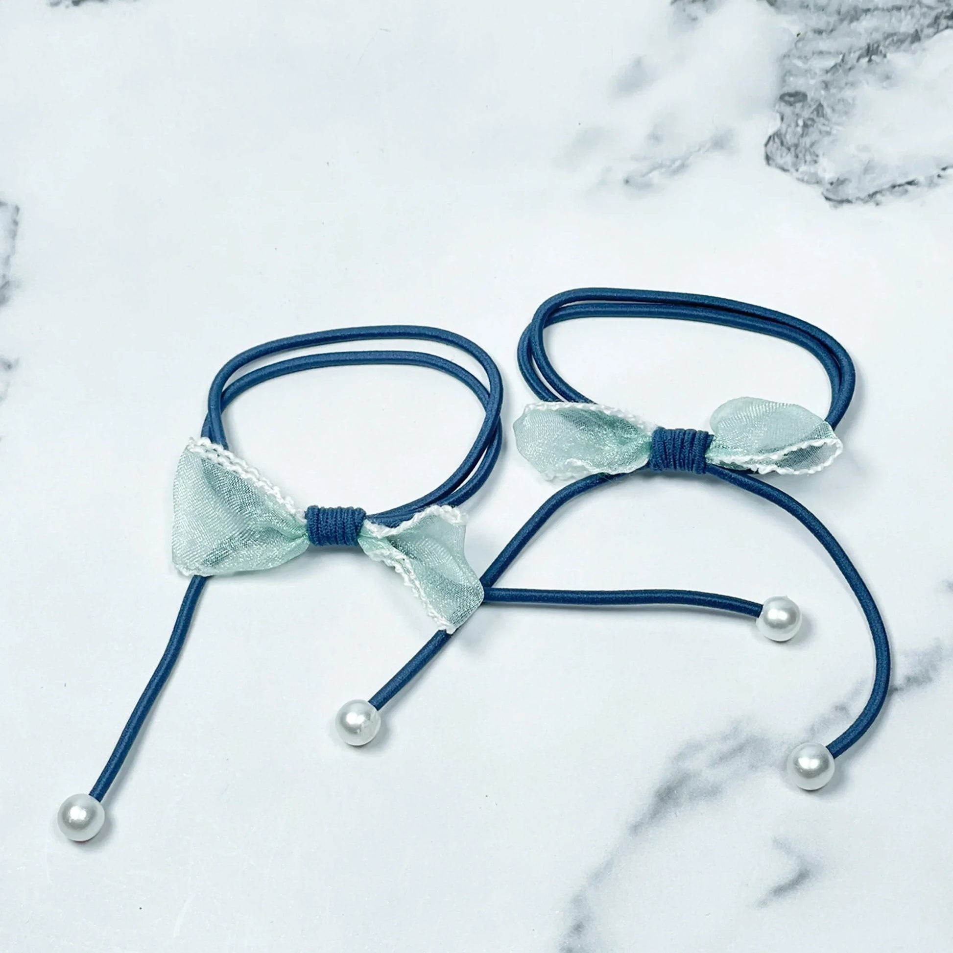 Blue hair ties with bows and beads featuring pearl-like accents on a marble background