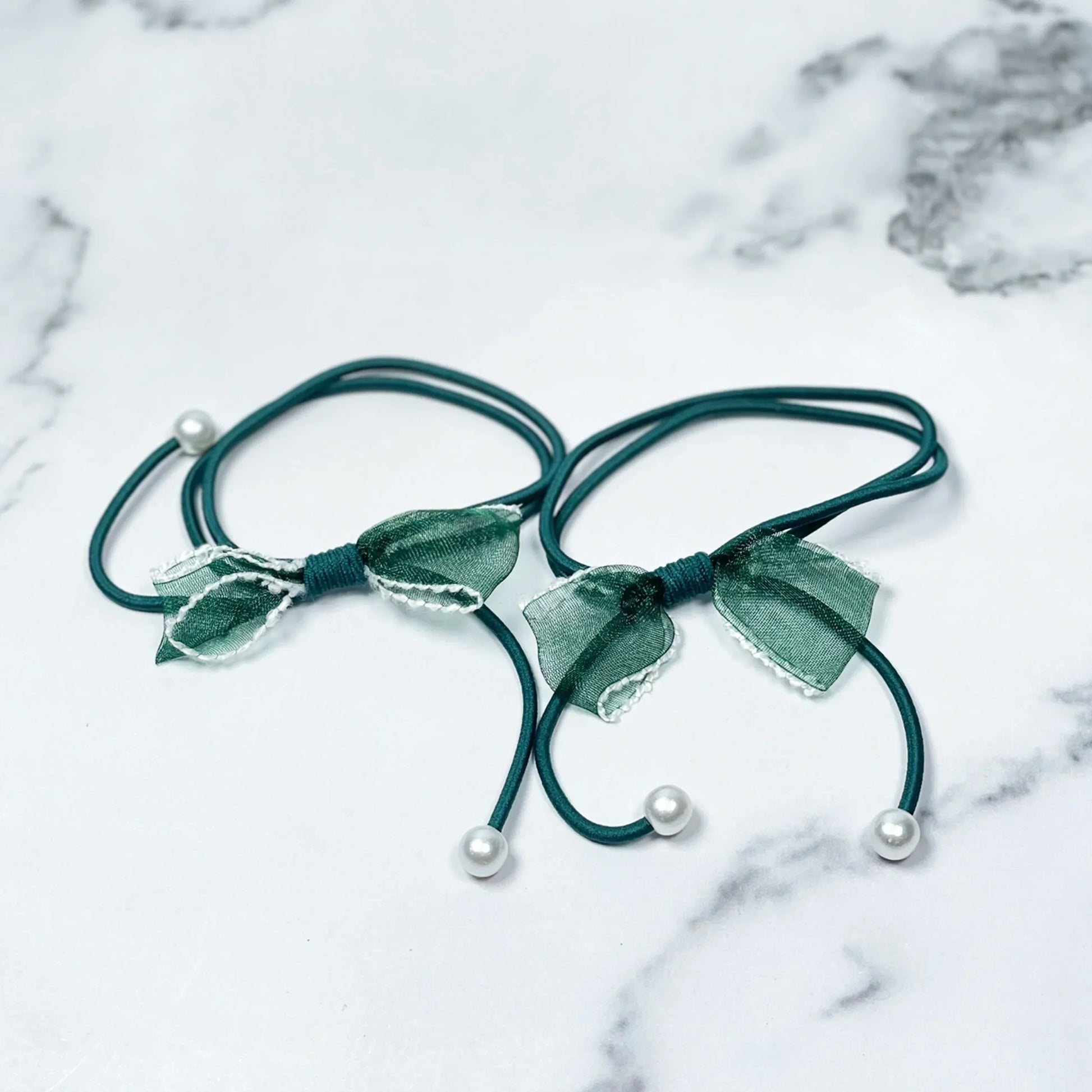 Green hair ties with bows and beads on a white marble surface from mydevelopmentstor