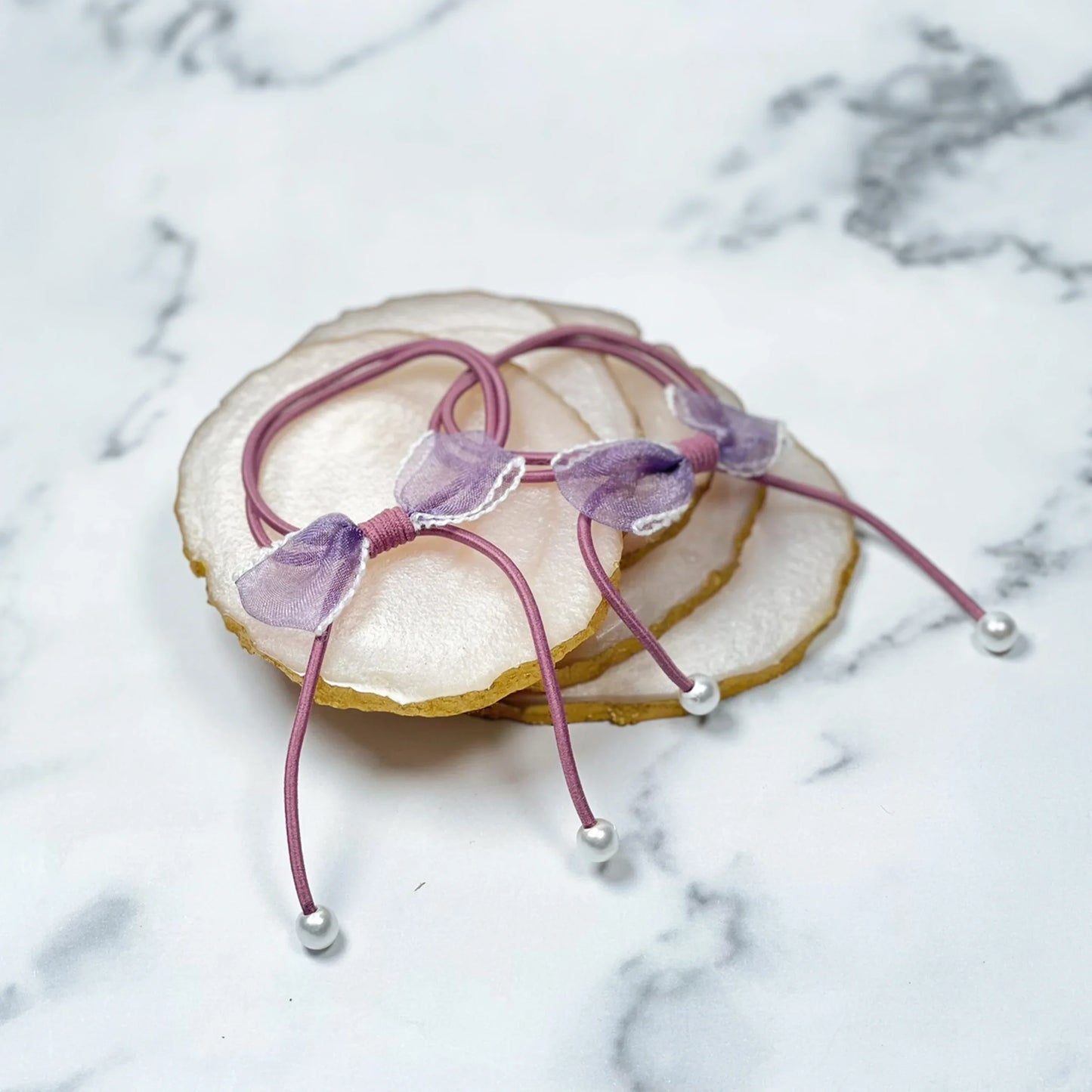 Purple hair ties with bows and beads on a marble surface and agate coasters