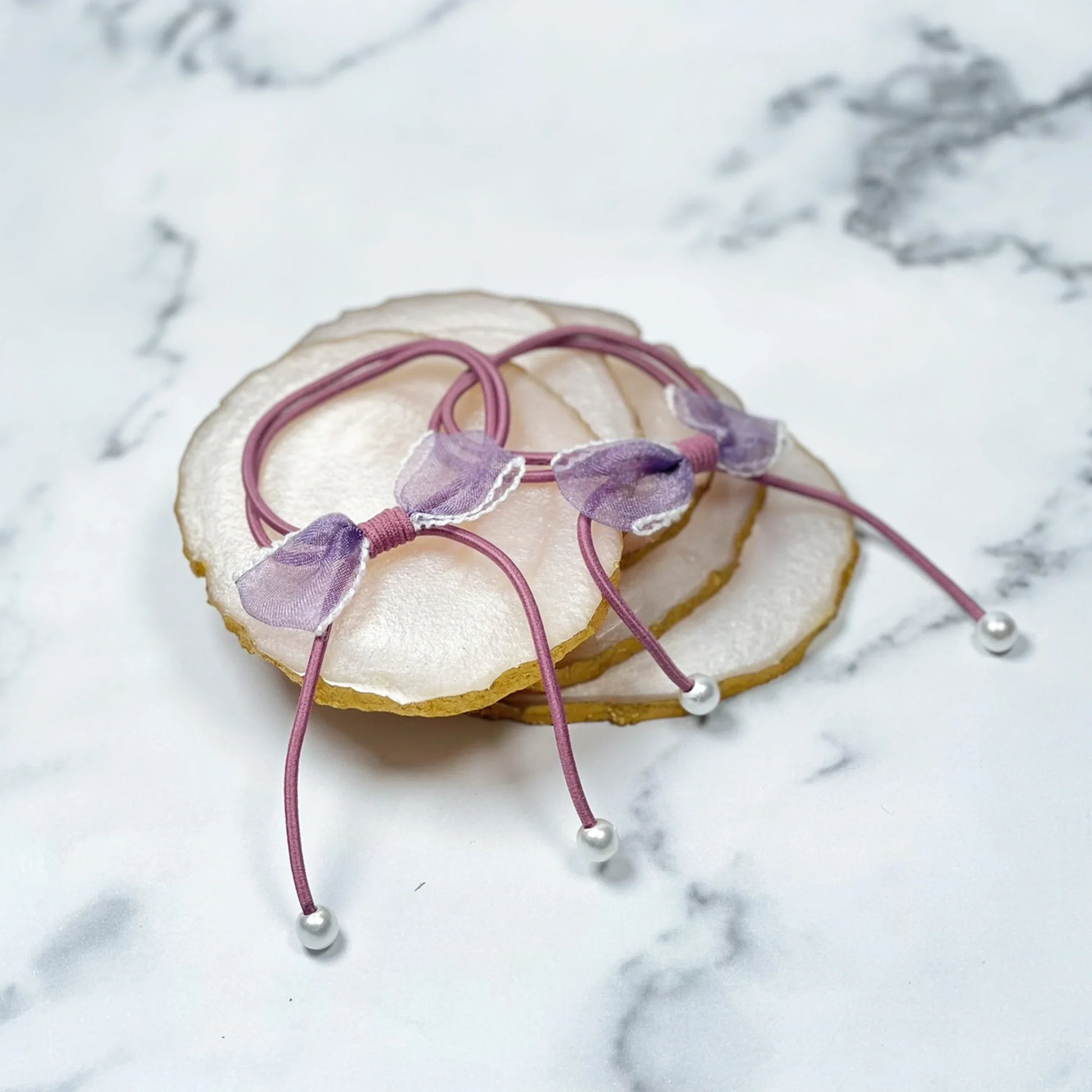 Purple hair ties with bows and beads on a marble surface and agate coasters